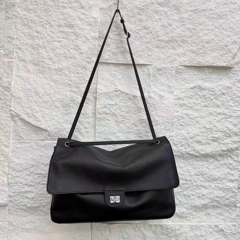 Back view of a black leather handbag featuring a stitched exterior pocket, premium textured leather surface, adjustable shoulder strap, and refined edge finishing. The minimalist back design highlights handcrafted quality, durability, and practical storage. This elegant leather purse combines classic style with everyday functionality, making it perfect for modern fashion, work, travel, and casual outings.