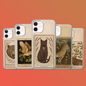 May include: A set of phone cases with tarot card illustrations. The designs include a bear, owl, cat, wolf, and deer. Each case has a beige border, and the tarot card images are framed with botanical elements. The text on the cards is visible.