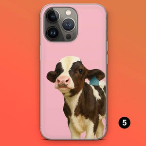 May include: A pink phone case featuring a brown and white calf with a blue ear tag. The calf has a pink nose and is set against a pink background. The phone case has a clear border and a camera cutout.