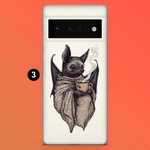 May include: A phone case featuring a whimsical illustration of a bat wrapped in a blanket, holding a steaming cup of coffee. The bat is depicted in shades of gray and brown, with a small cup featuring a camel silhouette.