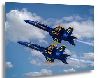 May include: Two blue and yellow U.S. Navy Blue Angels fighter jets flying in formation against a bright blue sky with white clouds. The jets are marked with the numbers 5 and 6, the text Blue Angels, and U.S. Navy on the wings and tail fins.