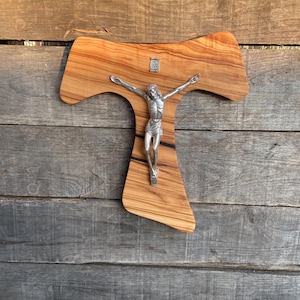 May include: A wooden crucifix with a silver-toned Jesus figure. The cross is made of olive wood, with a natural grain pattern. The figure of Jesus is detailed, with outstretched arms. The letters "INRI" are visible above the figure.