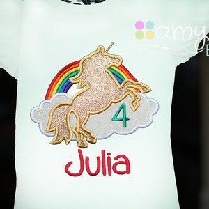 May include: White t-shirt with a gold glitter unicorn, rainbow, and clouds. The number 4 and the name Julia are embroidered on the shirt.