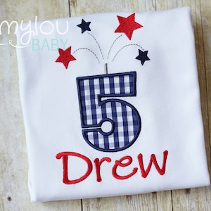 May include: White t-shirt with a blue and white checkered number 5, red fireworks, and the name "Drew" embroidered in red.