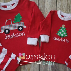 May include: Red and white striped pajamas with a red long-sleeved shirt featuring a green Christmas tree and a red truck with a plaid design. The shirt is personalized with the name "Jackson". The second pajama set is red and white striped with a red long-sleeved shirt featuring a green Christmas tree with white polka dots. The shirt is personalized with the name "Charlotte".