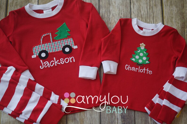 May include: Red and white striped pajamas with a red long-sleeved shirt featuring a green Christmas tree and a red truck with a plaid design. The shirt is personalized with the name "Jackson". The second pajama set is red and white striped with a red long-sleeved shirt featuring a green Christmas tree with white polka dots. The shirt is personalized with the name "Charlotte".