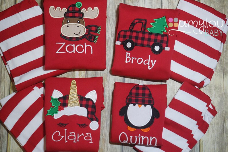 May include: Four red and white striped shirts with different embroidered designs. The designs include a moose, a truck with a Christmas tree, a unicorn, and a penguin. Each shirt has a name embroidered on it: Zach, Brody, Clara, and Quinn.
