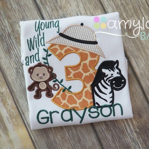 May include: White t-shirt with a green, brown, and orange embroidered design. The design features a giraffe-print number 3, a monkey, a zebra, and the text "Young Wild and Grayson".