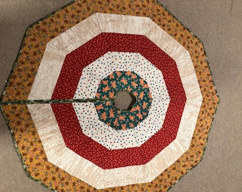 May include: A colorful Christmas tree skirt with a circular design. The skirt features concentric rings of red, white, green, and gold fabrics. The center ring is green with gingerbread men. The outer edge has a leaf pattern.