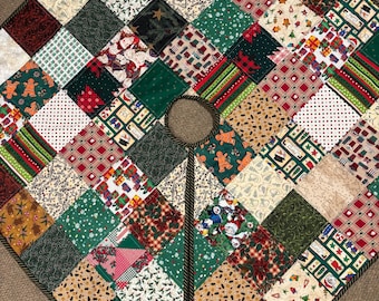 May include: A patchwork Christmas tree skirt with a variety of festive patterns. The skirt is octagonal, featuring squares of green, red, and beige fabrics with holiday motifs like gingerbread men, stars, and presents. A dark brown rope trim edges the skirt.