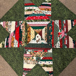May include: A handmade Christmas-themed quilted table topper. The topper features a central star design with various fabric strips in red, green, white, and gold. The outer border is a solid green fabric with a swirling pattern. The overall design is festive and decorative.