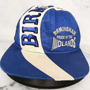 Op de afbeelding: Een blauwe baseballcap met een witte streep en het woord "BIRM" geborduurd in blauw. De cap heeft ook de tekst "Birmingham Pride of the Midlands" in wit. De cap heeft een gebogen klep.