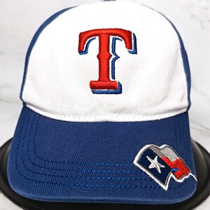 May include: A blue and white baseball cap with a red and blue embroidered "T" logo. The cap has a blue peak and a Texas flag patch.