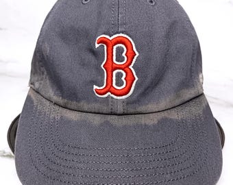 May include: A grey baseball cap featuring a red and white embroidered "B" logo. The cap has a curved peak and an adjustable strap. The hat is made of a durable fabric.