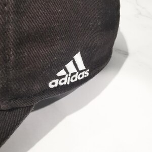Puede incluir: Gorra de b&eacute;isbol marr&oacute;n oscuro con el logotipo de Adidas bordado en blanco en el lateral. La gorra est&aacute; hecha de una tela texturizada y tiene una visera curva.