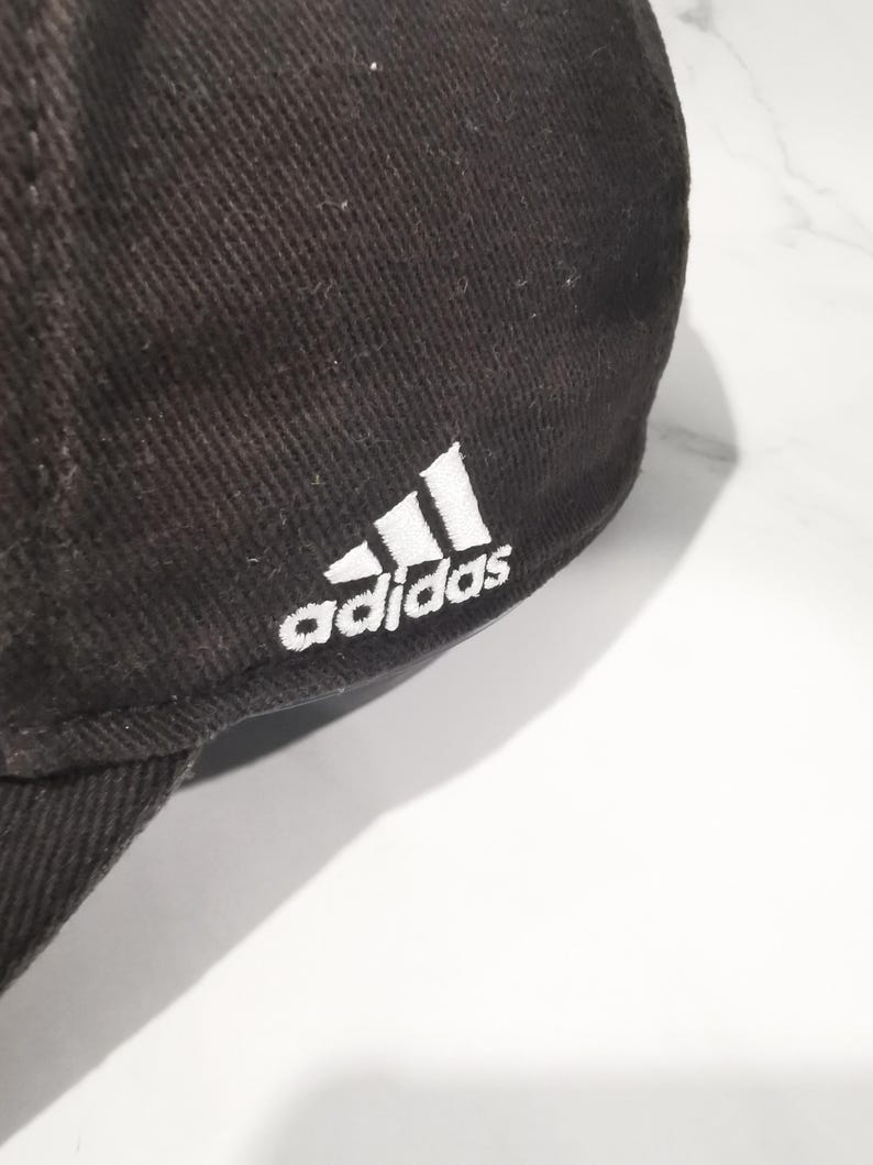 Puede incluir: Gorra de b&eacute;isbol marr&oacute;n oscuro con el logotipo de Adidas bordado en blanco en el lateral. La gorra est&aacute; hecha de una tela texturizada y tiene una visera curva.