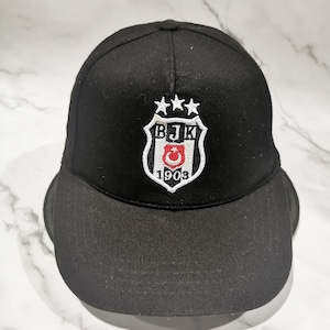 May include: Black baseball cap with a curved brim. The cap features a white embroidered emblem with the letters "BJK", three stars, a crescent moon, and a star. The number "1903" is also embroidered on the emblem.