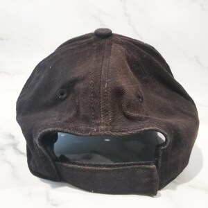 Puede incluir: Gorra de b&eacute;isbol negra con visera curva y correa ajustable. La gorra est&aacute; hecha de una tela texturizada y tiene un bot&oacute;n en la parte superior. La parte trasera de la gorra es visible, mostrando la correa ajustable.