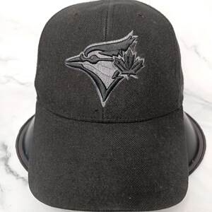 May include: Black baseball cap with the Toronto Blue Jays logo embroidered on the front. The logo features a stylized bird and a maple leaf in grey tones. The cap has a curved peak and a structured design.