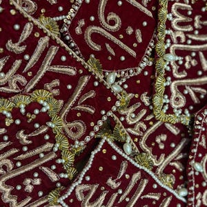 Op de afbeelding: Close-up van verschillende sierlijke, dieprode fluwelen vierkanten met gouden borduursels en witte parelaccenten. De vierkanten hebben ingewikkelde patronen en script. Het algehele ontwerp is rijk en gedetailleerd.