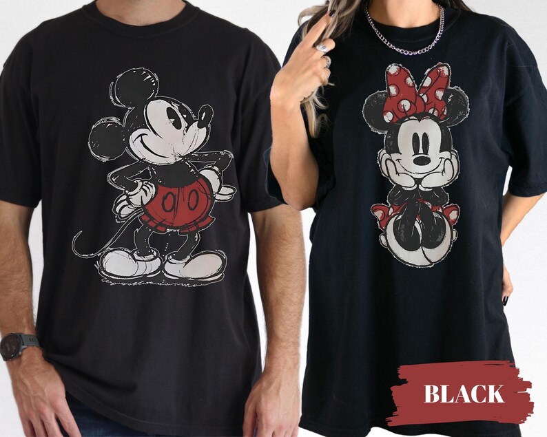 May include: Black t-shirts featuring Mickey Mouse and Minnie Mouse. Mickey is in a red shorts and Minnie is wearing a red bow. The graphic design has a distressed, vintage look. The word "BLACK" is in a red rectangle.