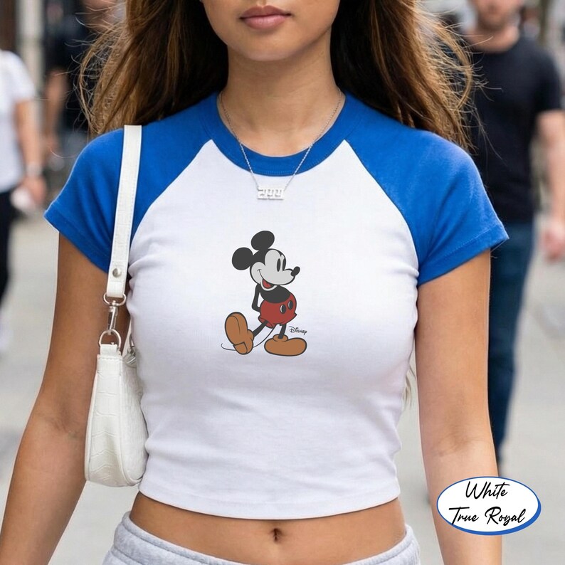 May include: White and royal blue raglan style crop top featuring a Mickey Mouse graphic. The shirt has a white body with royal blue sleeves and neckline. The Mickey Mouse design is in classic colors.
