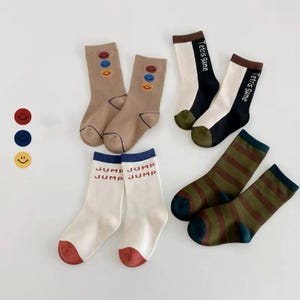 Può includere: Una collezione di calzini colorati con vari disegni. Due paia di calzini color beige con faccine sorridenti. Due paia di calzini con la scritta "Tetris Game". Due paia di calzini a righe sono verdi e marroni. Due paia di calzini bianchi con la parola "JUMP".