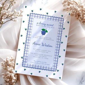 May include: A baby shower invitation with a blueberry theme. The invitation has a blue and white gingham border and the text "a berry sweet BABY IS ON THE WAY". The invitation includes the name Anne Weston and event details.