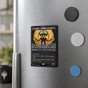 May include: A rectangular magnet featuring the Magic: The Gathering card Sheoldred, the Apocalypse. The card art displays a central figure with horns and a red outfit against a golden circular background, with text detailing the creature's abilities.