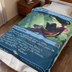 May include: A rectangular fleece blanket featuring a large-scale print of the Magic: The Gathering card Rhystic Study. The design displays a blue border, the title Rhystic Study, and an illustration of a merfolk figure reading a book underwater.