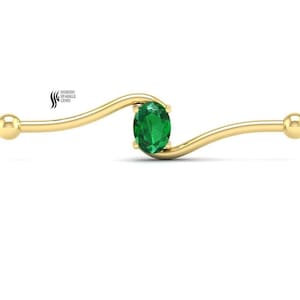 May include: A gold industrial barbell with a curved bar and a central oval-cut green gemstone held by four prongs. The ends of the barbell feature smooth, round spheres. The text "SHIRISH SPARKLE GEMS" is visible in the upper left corner.