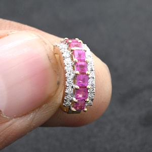 May include: A gold-toned hoop earring featuring a row of vibrant pink gemstones, accented with smaller, sparkling white stones. The gemstones are set in a continuous band, creating a luxurious and eye-catching design. Jewelry.