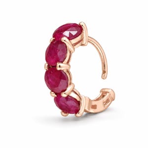 Peut inclure: Une créole en or rose ornée de quatre rubis ronds à facettes d'un rouge profond, disposés en rangée verticale sur la courbe avant. L'anneau en métal présente une finition polie et un mécanisme à charnière, offrant un design classique et élégant.