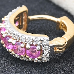 May include: A gold and silver earring with pink gemstones and small clear stones. The earring has a hinged design and is set with multiple pink gemstones and clear stones. The metal is a mix of gold and silver.