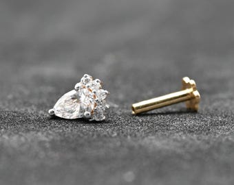 May include: A gold-colored earring stud with a pear-shaped clear gemstone and several smaller clear gemstones clustered around it. The earring post is separate. Jewelry.
