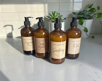 May include: Four amber glass bottles with black pump dispensers, each featuring a beige label with the text Sage Apothecary and specific scent names: Fragrance Free, Crisp Agave, Sanctuary, and Ritual, with 16 oz printed on each label.
