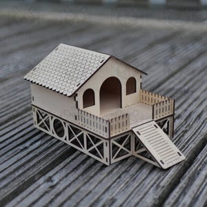 Può includere: Una piccola casetta di legno per criceti, con tetto spiovente, porta ad arco e un piccolo terrazzo con rampa. La casa è costruita in legno chiaro e presenta intagli decorativi.