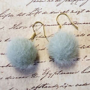 May include: A pair of earrings with light gray fluffy pom poms and gold hooks.