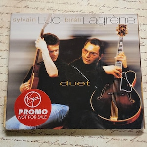 May include: A promotional CD cover featuring two musicians, Sylvain Luc and Biréli Lagrène, playing guitars. The cover is red and black with the title "duet" in yellow text. The CD is a promo copy and is not for sale.
