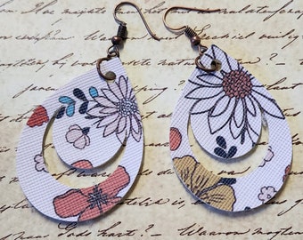 May include: A pair of white teardrop-shaped earrings with a floral pattern. The earrings are layered with two teardrop shapes, one inside the other. The earrings have a copper-colored hook.