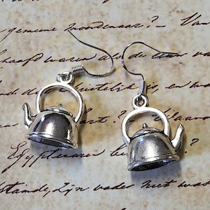 May include: A pair of silver teapot earrings. The teapots have a shiny, metallic finish and are detailed with a spout, handle, and lid.