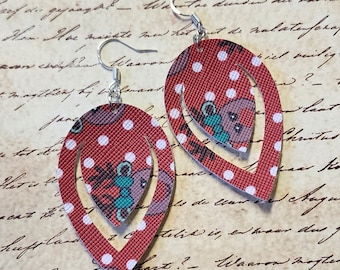May include: A pair of red and white polka dot dangle earrings with a smaller teardrop-shaped earring inside. The earrings are made of leather and have a silver hook.