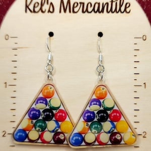May include: A pair of silver-toned dangle earrings. Each earring features a triangular design with a pool ball rack arrangement. The earrings display a variety of colorful pool balls, including yellow, red, blue, and black.