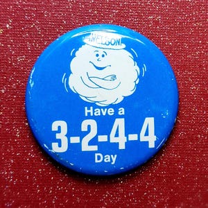 May include: Blue and white button with a cartoon cloud character wearing a hat and the text "Have a 3-2-4-4 Day".