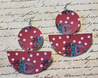 May include: A pair of red and white polka dot earrings with a reindeer design. The earrings are made of fabric and have a silver hook closure.