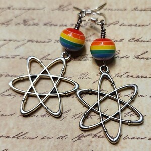 May include: Silver atom earrings with rainbow colored glass beads. The beads have red, orange, yellow, green, blue, indigo, and violet stripes.