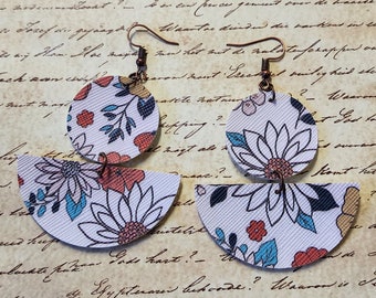 May include: A pair of floral patterned earrings with a white background and colorful flowers. The earrings are made of leather and have a semi-circle shape with a smaller circle on top.