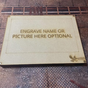 May include: A rectangular, light-brown wooden plaque with the text "ENGRAVE NAME OR PICTURE HERE OPTIONAL" engraved in the center. The Laser Raven logo is in the bottom right corner. The plaque is on a patterned surface.
