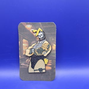 Puede incluir: Un pin que presenta una figura con cara de calavera con un disfraz de conejito, con un body de red negro. El pin tiene detalles amarillos y beige, y está montado en una tarjeta con un fondo de escena de bar. El pin está sobre un fondo azul.