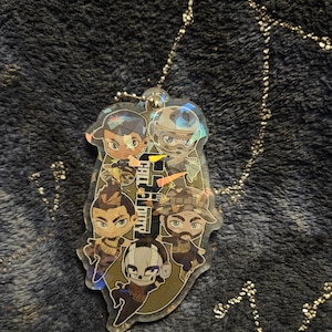 May include: A clear acrylic keychain featuring cartoon characters from the video game "Call of Duty." The keychain has a silver chain and a silver ball at the top. The characters are in various poses, with the game's logo in the center.